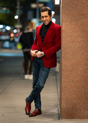 Man in a red blazer standing against a wall on a city street.