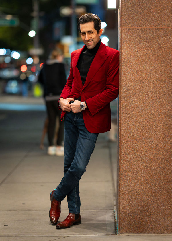 Man in a red blazer standing against a wall on a city street.