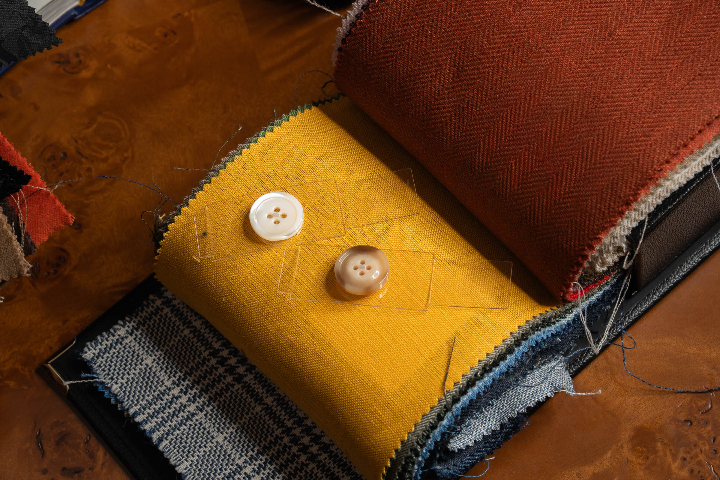 Fabric swatches in yellow, brown, and blue with buttons on a wooden surface