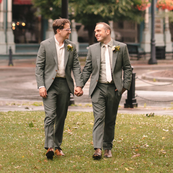 Two men in suits walking hand in hand on a grassy area with a blurred background