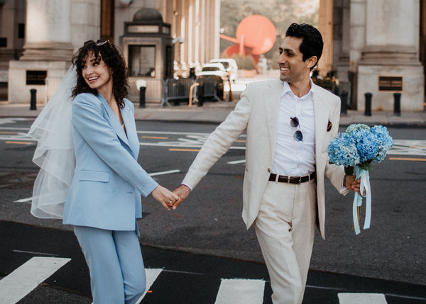 Couple holding hands on a city street with a large archway in the background.