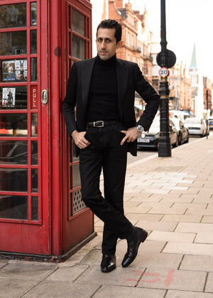 Man in a black suit standing next to a red telephone booth on a city street.