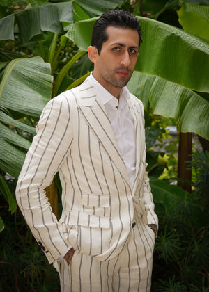 Man in a white pinstripe suit standing in front of large green leaves