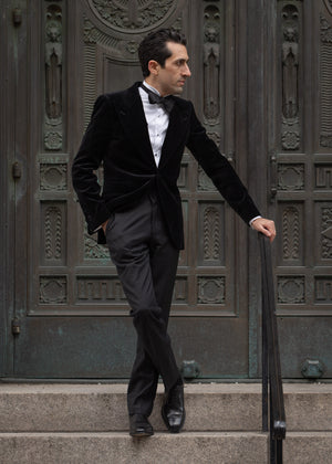 Man in a black suit standing on steps in front of an ornate door.
