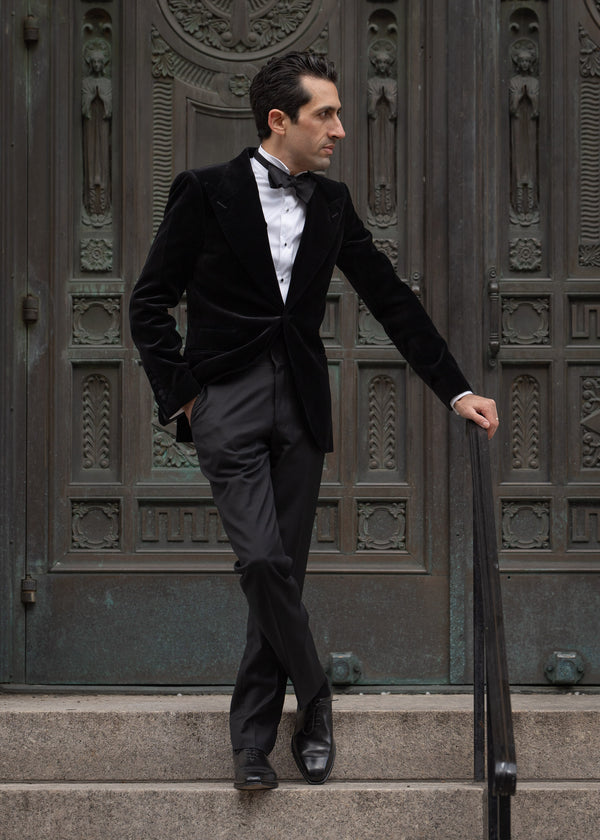 Man in a black suit standing on steps in front of an ornate door.