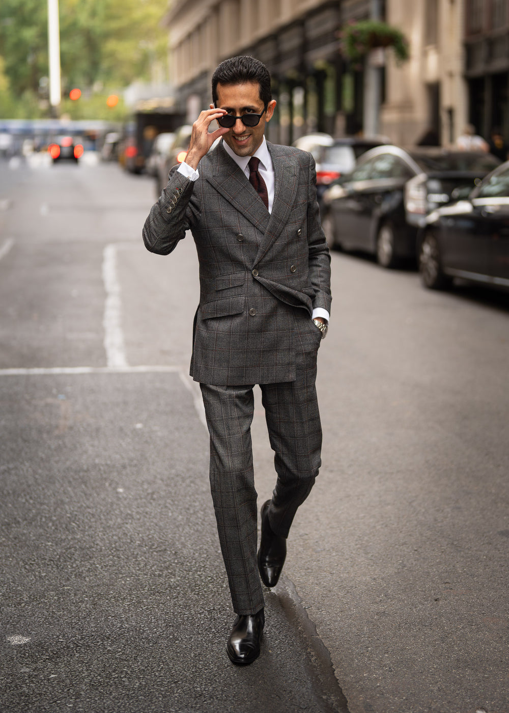 Man in a blue suit sitting on a pipe, talking on a phone, with graffiti in the background.