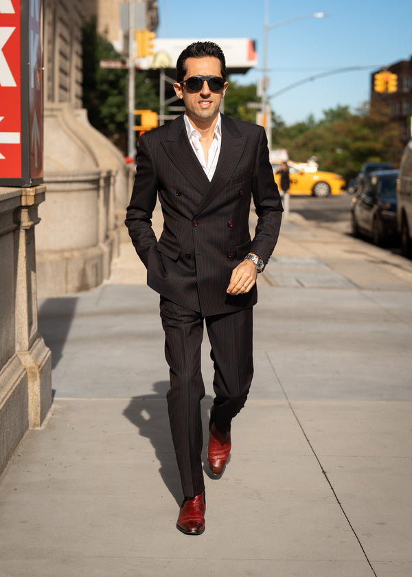 Man in a black suit with red shoes walking on a city street.