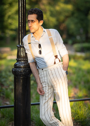 Man in suspenders and striped pants leaning against a lamp post outdoors