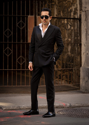 Man in a black suit standing in front of a textured wall.