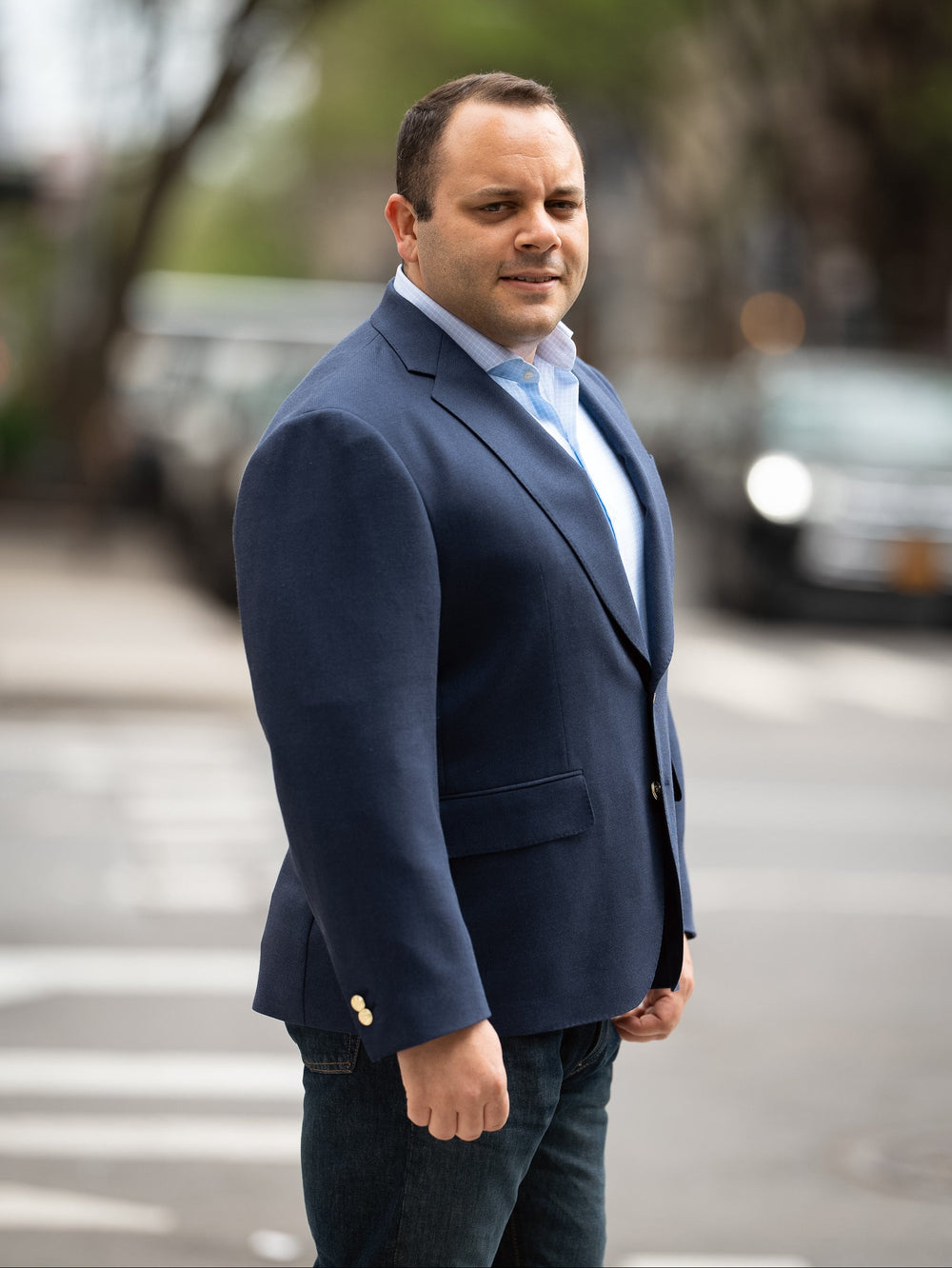 A man in a blue blazer standing with his arms by his side.