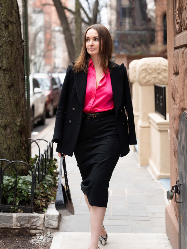 Woman walking down the street wearing a pink shirt, black skirt and black blazer.
