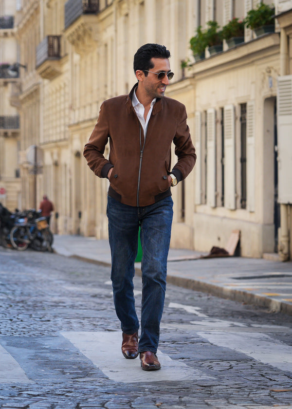 Man walking on a street wearing a brown jacket and blue jeans.
