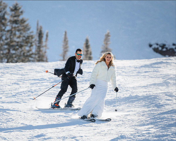 Two people skiing on a snowy slope with trees in the background