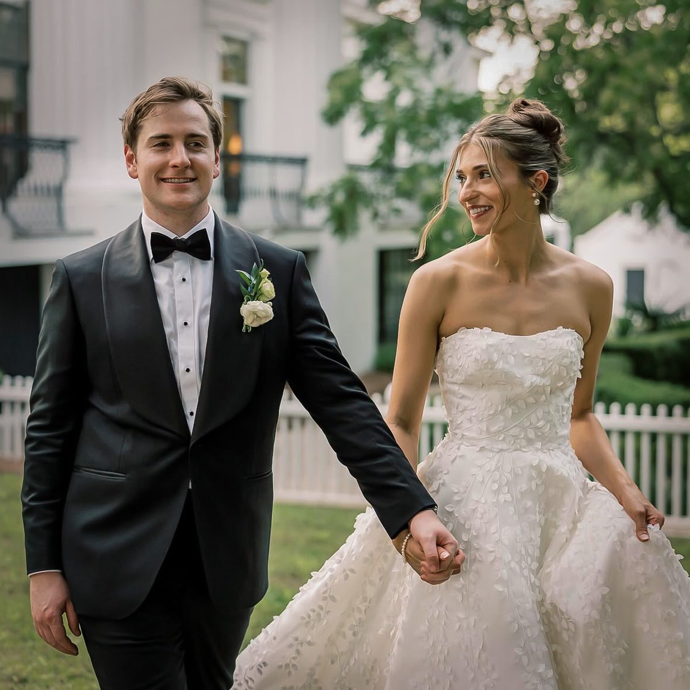Man in tuxedo and woman in wedding dress holding hands outdoors.