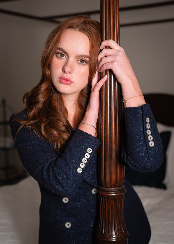 Woman in a dark blue coat with white buttons holding a wooden post indoors.