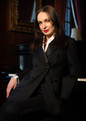 Woman in a black coat sitting in a room with a mirror and lamp.