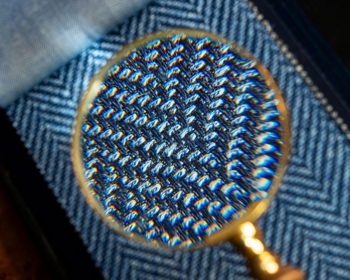 A close-up view through a magnifying glass showing the detailed blue and white herringbone knit pattern of a sweater.