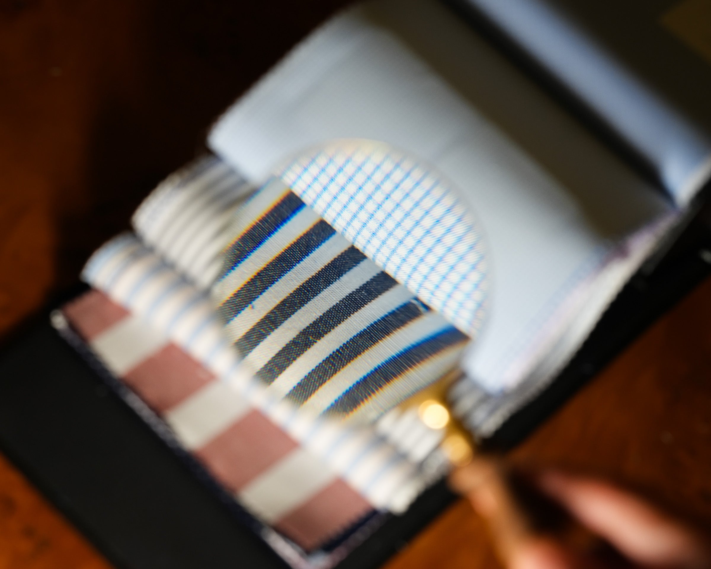 A close-up of a fabric sample book or card set on a dark surface, showing folded striped and checkered textile samples in blue, beige, brown, and white tones.